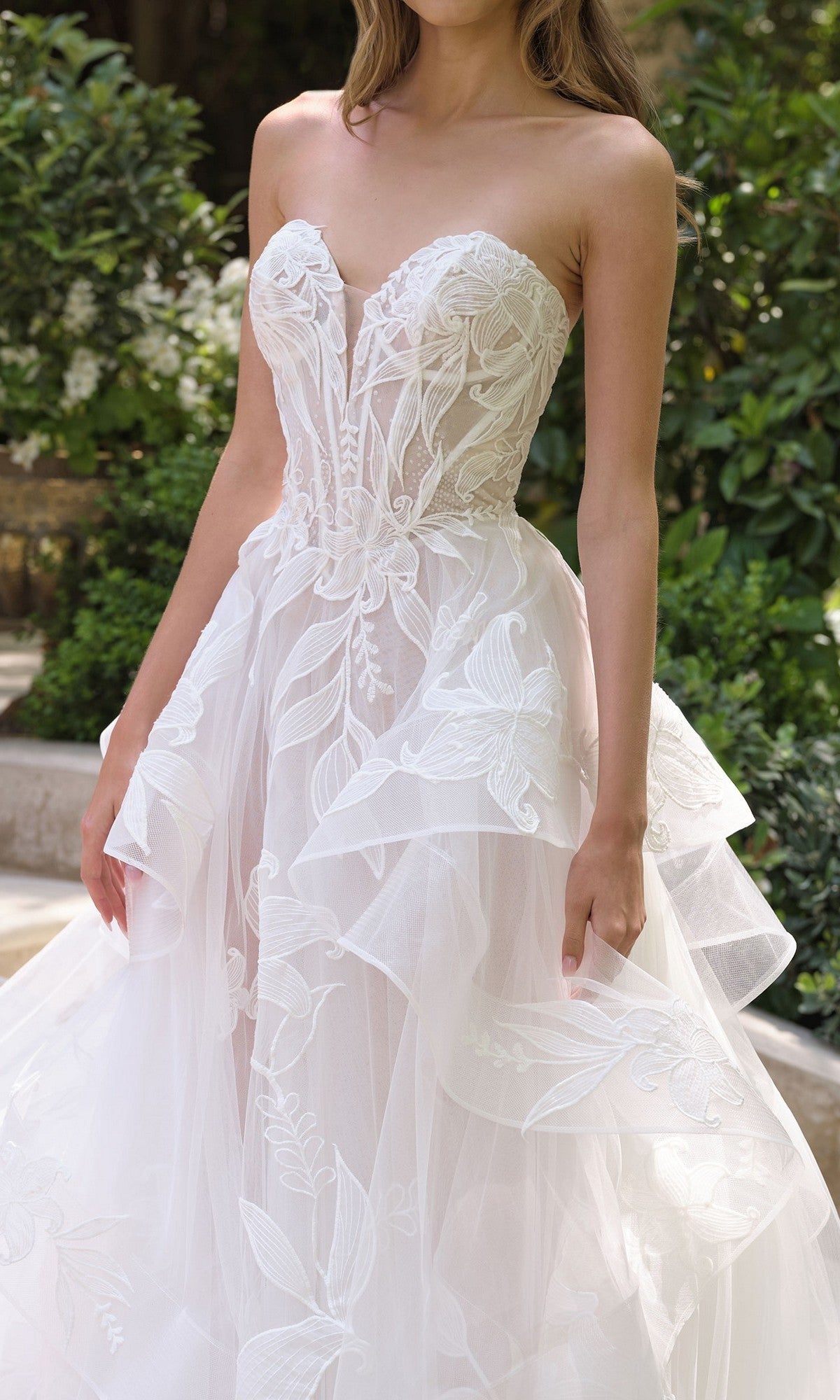 A woman stands outdoors in the Andrea and Leo WL059 long white wedding dress, featuring a strapless fitted bodice, floral lace details, and a layered tulle skirt for timeless elegance.